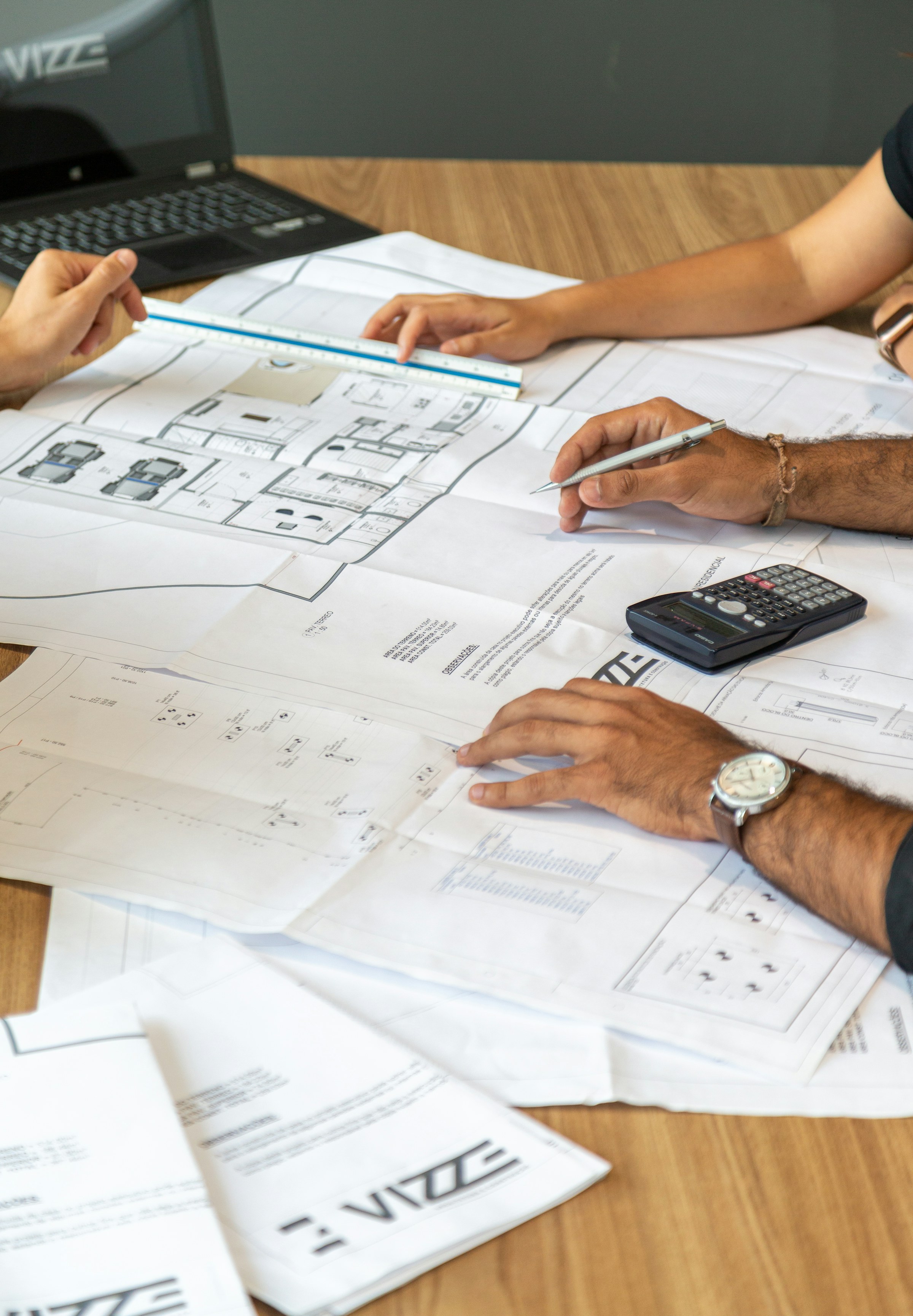 People reviewing architectural plans and drawings together at a desk with a calculator and laptop.